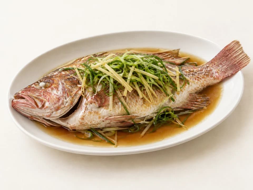 A whole steamed grouper with ginger and spring onion on a platter